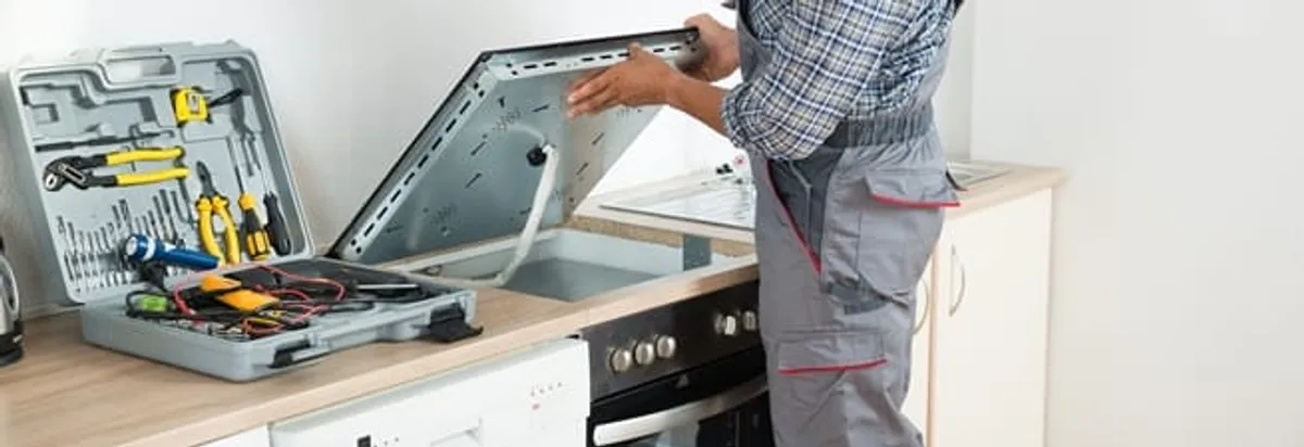 Cooktop repair technician lifting a built-in stovetop for service in Mobile, AL