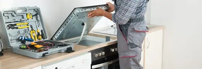 Cooktop repair technician lifting a built-in stovetop for service in Mobile, AL