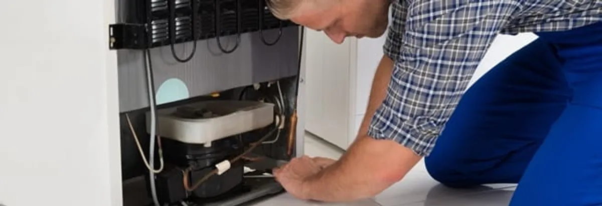 Refrigerator repair technician servicing the compressor and condenser area in Mobile, AL