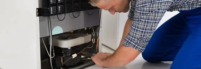 Refrigerator repair technician servicing the compressor and condenser area in Mobile, AL