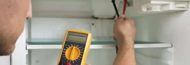 Refrigerator repair technician testing electrical components with a multimeter in Mobile, AL